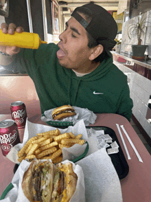 a man is eating a hamburger and french fries with a can of dr. pepper on the table