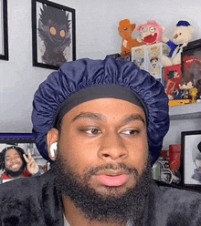 a man with a beard wearing a blue hat is sitting in front of a shelf filled with stuffed animals .