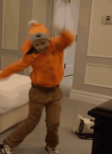 a young boy wearing an orange jacket and a white hat is dancing