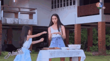 a woman and a little girl are standing next to a table with food on it in front of a house .