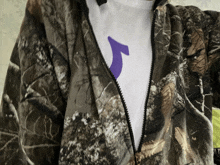 a person wearing a camo jacket and a white shirt with a purple letter j on it