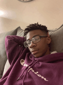 a young man wearing glasses and a purple champion hoodie lays on a couch