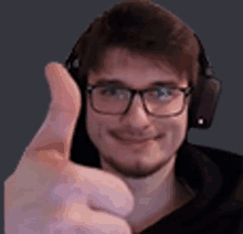 a young man wearing headphones and glasses is giving a thumbs up .