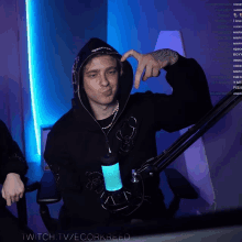 a man in a black hoodie stands in front of a microphone with the hashtag twitch.tv/ecorkreed visible