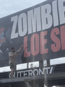 a man points to a large billboard that says zombie loes