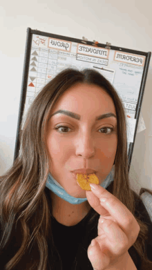 a woman wearing a mask is eating a chip in front of a board that says " word "