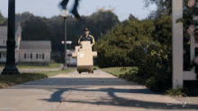 a man is pushing a cart full of boxes down a sidewalk with a disney + logo in the background