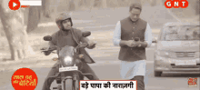 a man riding a motorcycle next to another man with gnt written on the bottom of the screen