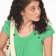 ariana grande is wearing a green shirt and a white purse .