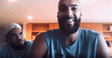 a man with a beard is smiling while another man looks on in a video call .