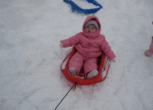 a baby in a pink outfit is sledding down a snowy hill