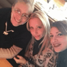 three women are posing for a picture while sitting at a table in a restaurant .