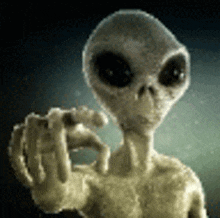 a gray alien is pointing at the camera with his finger .