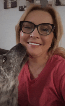 a woman wearing glasses and a pink shirt is kissed by a dog