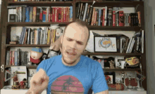 a man in a blue shirt is standing in front of a bookshelf filled with books including one that says creative rogue