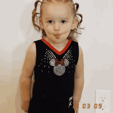 a little girl wearing a black minnie mouse tank top with rhinestones on it