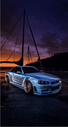 a silver sports car is parked in front of a boat at sunset