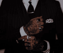 a man in a suit and tie has a lot of tattoos on his hands and arms .