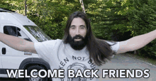 a man with long hair and a beard is standing in front of a van with the words welcome back friends written below him