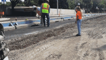 a group of construction workers are working on a road and one of them is wearing a yellow vest with the word safety on it