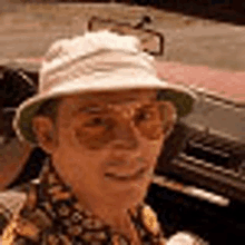 a man wearing a hat and sunglasses is standing in front of a car .