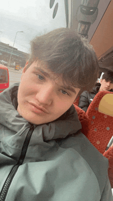 a man in a grey jacket is sitting in a red seat on a bus