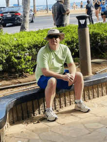 a man wearing a hat and sunglasses sits on a stone bench