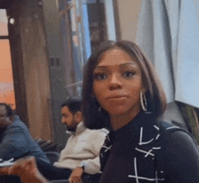 a woman wearing hoop earrings looks at the camera while sitting in a chair