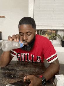 a man wearing a red bulls shirt is drinking water from a bottle