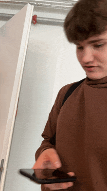 a man in a brown shirt is holding a cell phone in front of a door