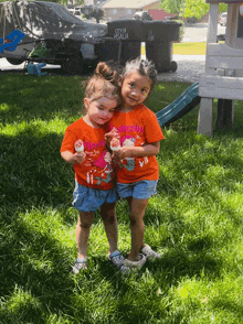 two little girls are standing in the grass wearing orange shirts that say mom