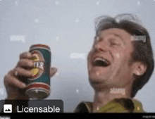 a man is laughing while holding a beer can in his hand .