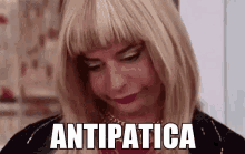 a woman in a wig is making a funny face and the word antipatica is written on her face .