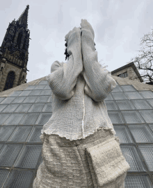 a person covering their face with their hands in front of a building with a steeple in the background