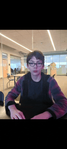 a boy wearing glasses is sitting at a table in a room with a sign that says ' microsoft ' on it