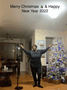 a woman stands in front of a christmas tree with her arms outstretched and the words merry christmas and happy new year 2022 above her