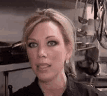 a close up of a woman 's face in a kitchen with pots and pans hanging on the wall .