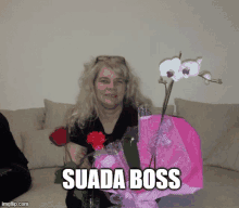 a woman sitting on a couch holding flowers and a pink bag that says suada boss