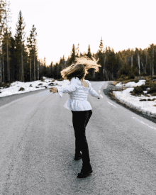 a woman in a white shirt and black pants is standing on a road with her arms outstretched