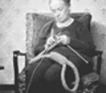 a woman is sitting in a chair knitting a rope .