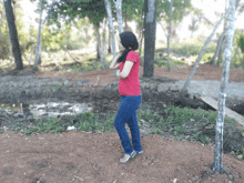 a girl in a red shirt and blue jeans is standing in the dirt