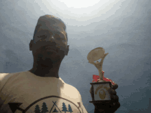 a man wearing a shirt with trees on it is holding up a trophy