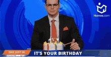 a man in a suit and tie is cutting a birthday cake in front of a sign that says it 's your birthday