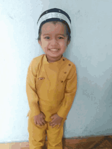 a little boy wearing a yellow shirt and a black hat is smiling for the camera