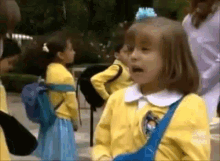 a little girl in a yellow jacket and blue skirt is standing in front of a group of children .