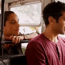 a man and a woman are sitting next to each other on a bus and looking out the window .