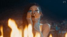 a woman with blue nail polish is covering her face with her hands in front of a fire .