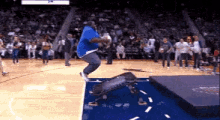 a man in a blue shirt is jumping in the air on a basketball court in front of a crowd