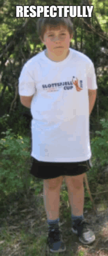 a boy wearing a slottsfjell cup shirt stands in the woods