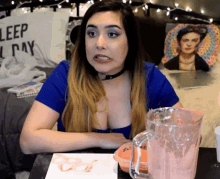 a woman in a blue shirt sits at a table in front of a sign that says sleep all day